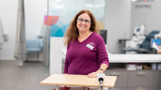 Smiling New York Blood Center staff member in a purple sweater at a blood drive.