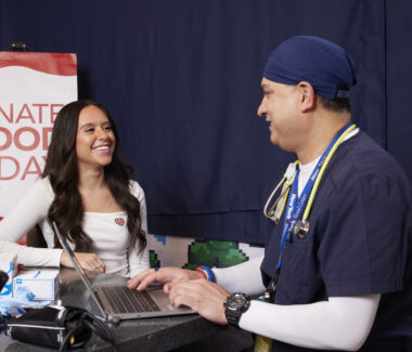 NYBC doctor discussing donation process with blood donor. Donate Blood Today sign is in the background.