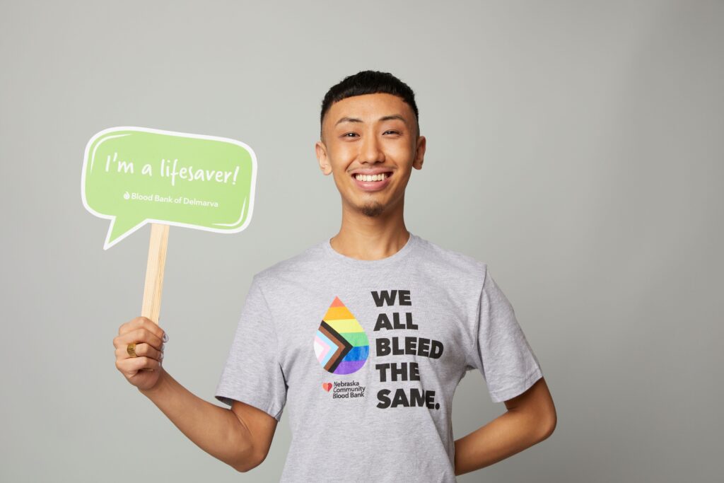 Image of person in a t-shirt reading We All Bleed the Same holding up a sign that reads I'm a Lifesaver.