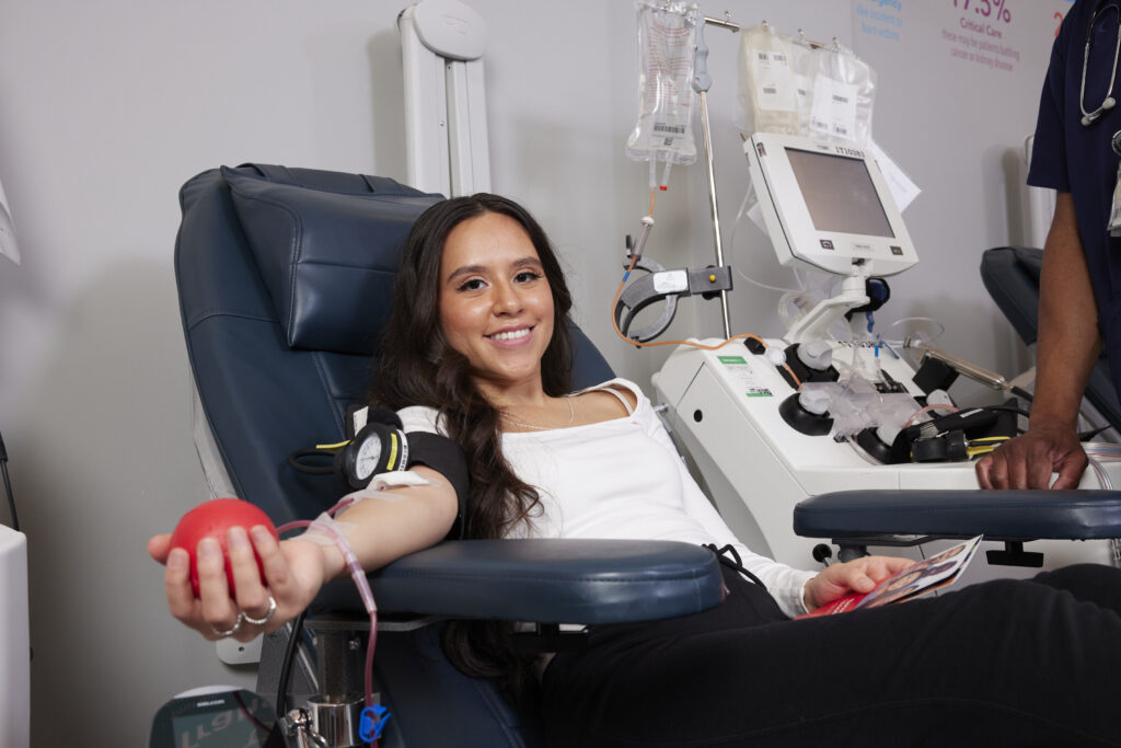 Smiling blood donor in donation chair squeezing a red foam heart.